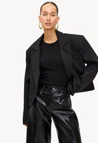 Blazer negro corto en tejido suave, combinado con una blusa negra de canalé y pantalones de pierna ancha con estampado de cocodrilo brillante. Pendientes de aro dorados.