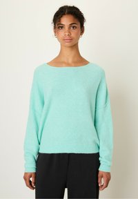Lys mintgrøn strikket sweater med en bred bådudskæring og lange ærmer. Blødt, struktureret stof falder løst over kroppen.