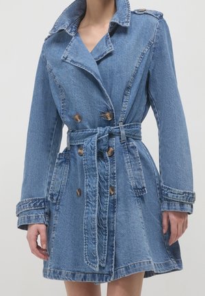 Vaaleansininen farkkutakki, jossa on vyöllinen vyötärö, kaksirivinen nappimalli ja suuret kaulukset. Teksturoitu kangas.