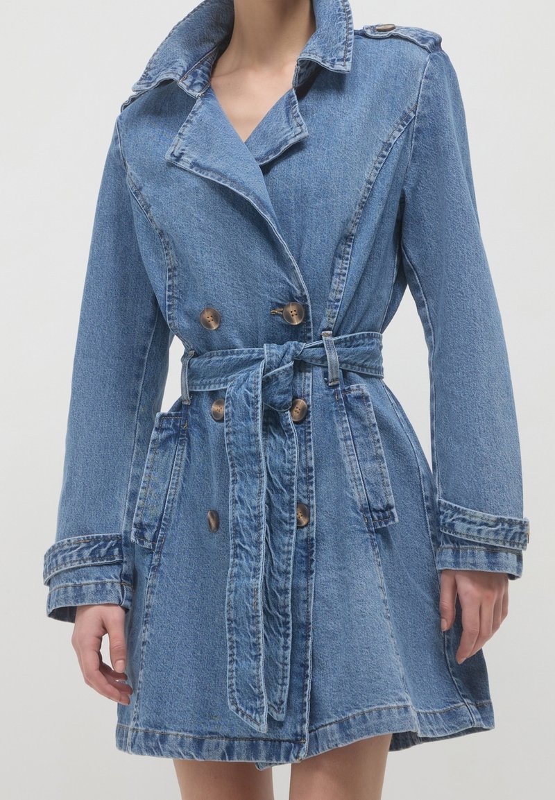 Denim trenčkot v světle modré barvě, s páskem v pase, dvouřadým zapínáním na knoflíky a velkými klopami. Texturovaná tkanina.