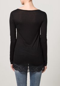 Camisa negra de manga larga con detalle de encaje en el dobladillo. Textura suave, tejido ligeramente transparente, escote redondeado y mangas ajustadas.