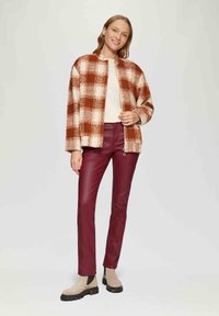 Kurtka w kratkę w kolorach pomarańczowym i kremowym, dopasowany kremowy top, burgundowe skórzane spodnie oraz beżowe botki z czarnymi podeszwami. Charakteryzuje się luźnym krojem i otwartym fasonem.