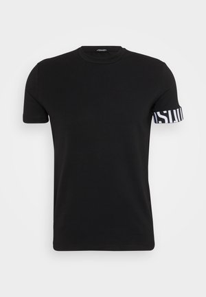 T-shirt noir à manches courtes en coton. Il présente un col rond et un accent rayé blanc sur la manche avec du texte. Texture lisse.