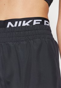 Mustat urheilushortsit, joissa on rypytetty vyötärö ja valkoinen Nike-logo. Pehmeä, kevyt materiaali, joka sopii aktiiviseen käyttöön.