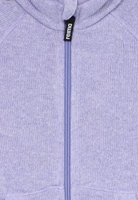 Hoodie en tricot lavande avec une fermeture éclair centrale et une étiquette noire « reima » attachée au tirette de la fermeture.