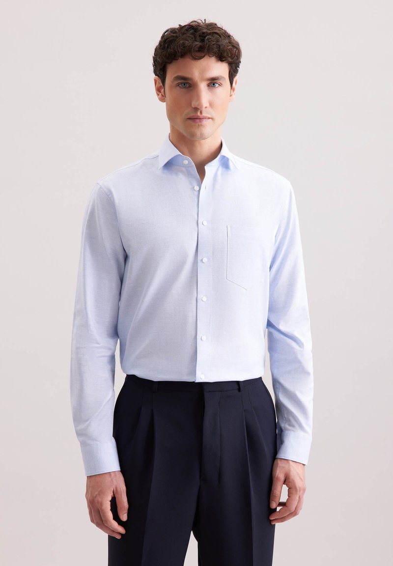 Camicia a maniche lunghe azzurra in tessuto strutturato con colletto button-down, taschino sul petto e bottoni bianchi. Abbinata a pantaloni scuri.