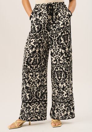 Black and white patterned wide-leg pants with an elastic waistband and side pockets, featuring a flowing fabric and contrasting accents.