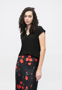 Melns tops ar īsām piedurknēm un V-veida izgriezumu ar mežģīņu detaļu, kopā ar melnu svārku ar sarkanu rožu apdruku. Gluda auduma tekstūra.