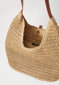 Wiklinowa torba na ramię w beżowym kolorze, z gładkim brązowym skórzanym paskiem i wewnętrzną kieszenią na zamek. Wytrzymała i pojemna konstrukcja.