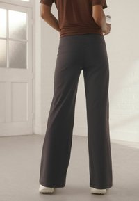 Platas kājas, tumšas bikses, izgatavotas no gludas materiāla ar augstu vidukli. Audums ir viegls, un biksēm nav redzamu rakstu vai rotājumu.