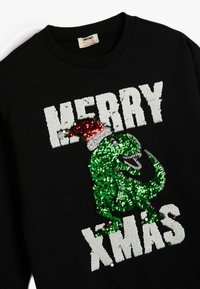 Sudadera negra con un T. rex de lentejuelas verdes que lleva un gorro de Santa rojo. "MERRY XMAS" en lentejuelas blancas en la parte frontal. Material de algodón.