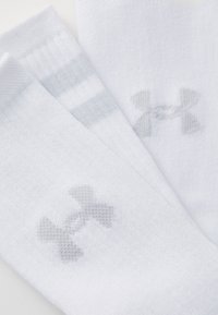 Biele športové ponožky so svetlošedými pruhmi a textúrovaným vzorom, s malým šedým logom Under Armour na každej ponožke.