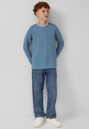 Langärmliges, hellblaues Baumwoll-T-Shirt mit einem weißen Rundhalsausschnitt, kombiniert mit locker sitzenden blauen Jeans und weißen Sneakers.