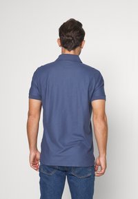 Polo shirt bleu marine avec un col, des manches courtes et une texture lisse. Porté avec un jean bleu clair. Design simple, sans motifs visibles.
