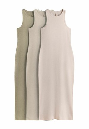 Sieviete bez piedurknēm gaiši rozā kleitā tur melnu džemperi un skatās uz sāniem pret vienkāršu baltu fonu.