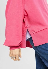 Rosa sweatshirt med ribbade muddar och nederkant, med sidofickor. Mjuk textur, avslappnad design. Bärs över en ljuslila lagertröja.