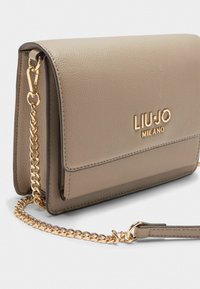 Beżowa skórzana torba na ramię z złotym łańcuszkiem, z klapką i wytłoczonym logo "LIU-JO MILANO" z przodu.