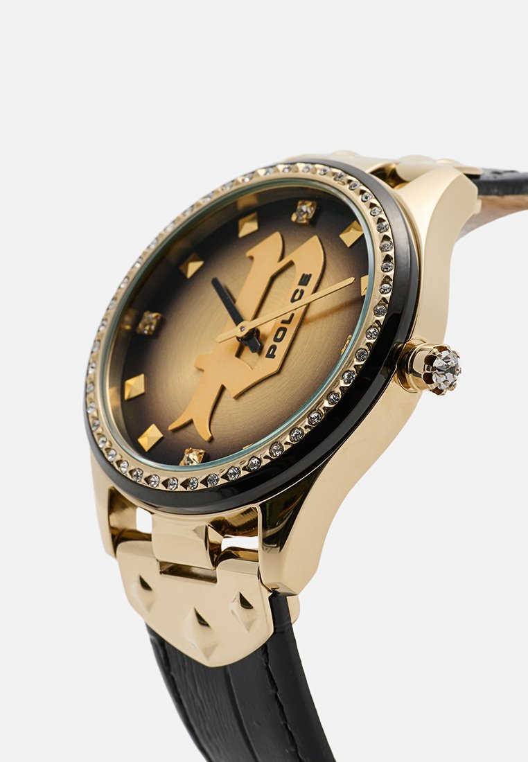 Reloj en tono dorado con una correa de cuero negra, esfera redonda con un rostro marrón degradado, acentos dorados y un bisel adornado con cristales.