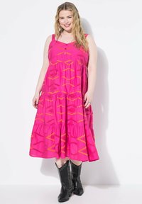 Fuchsia Baumwollkleid mit einem gestuften Design, das orange geometrische Muster und Knopfakzente aufweist. Getragen mit schwarzen, mit Nieten besetzten Stiefeletten.