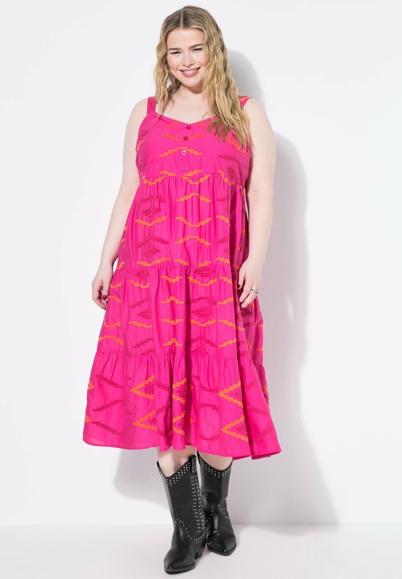 Fuchsia Baumwollkleid mit einem gestuften Design, das orange geometrische Muster und Knopfakzente aufweist. Getragen mit schwarzen, mit Nieten besetzten Stiefeletten.