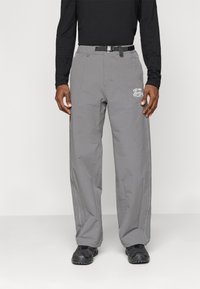 Sive hlače iz lahkega materiala imajo ravno krojenje, ojačane šive, črn pas in belo grafiko na levi nogi.