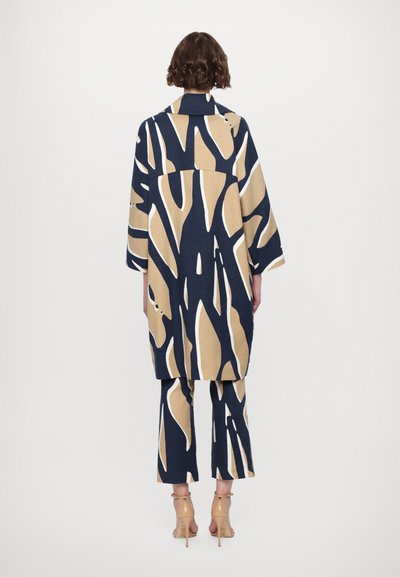 Navy blue and beige patterned oversized shirt and cropped pants set, made of fabric with a textured finish. Features wide sleeves and back details.