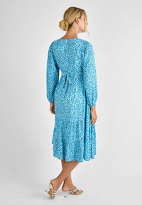 Blau gemustertes Kleid mit langen Ärmeln, Taillengürtel und gestuftem Rock. Der Stoff weist einen leichten, strukturierten Druck in unterschiedlichen Blautönen auf.