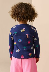 Námořnické žebrované tričko s dlouhým rukávem s barevným zvířecím a přírodním vyšíváním. Má vroubkovaný spodní lem a je kombinováno s růžovými šortkami.