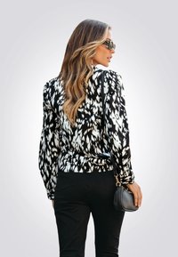 Zwart-witte geblokte blouse met lange mouwen, relaxte pasvorm, gecombineerd met zwarte broek. Accessoire: kleine zwarte handtas.