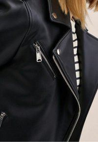 Veste de moto en cuir noir avec des fermetures éclair argentées, une fermeture éclair diagonale à l'avant et un col à pression. Caractérisée par un tissu texturé et une doublure rayée.