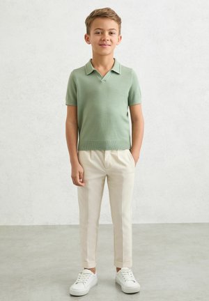 Tricou polo verde cu mâneci scurte tricotat, pantaloni crem croiți și adidași albi. Design simplu, material ușor și croială ajustată.