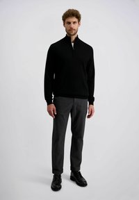 Schwarzer Reißverschluss-Pullover aus weichem Stoff, kombiniert mit dunklen grauen Hosen und schwarzen Lederschuhen mit Brogue-Details.