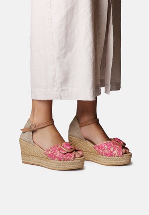 Dámske klinové sandále s ružovým kvetinovým vzorom a detailom mašle, pleteným podpätkom z jutového vlákna a svetlo béžovým pásikom okolo členka. Mäkká textúra a otvorená špička.