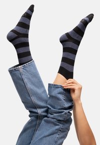 Des chaussettes rayées noires et bleues s'étendent à partir de jeans en denim retroussés, avec une texture lisse et un orteil et un poignet contrastants en noir.