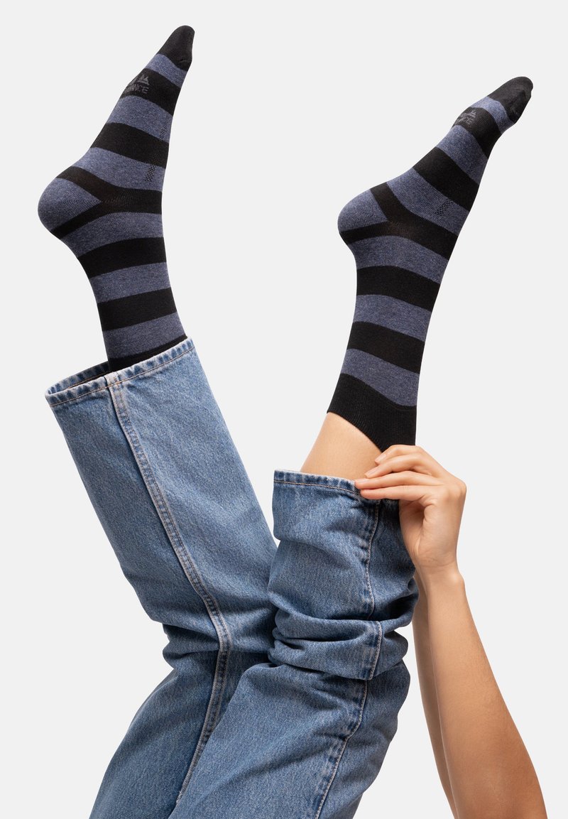 Des chaussettes rayées noires et bleues s'étendent à partir de jeans en denim retroussés, avec une texture lisse et un orteil et un poignet contrastants en noir.