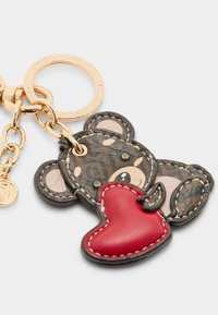 ATS PLECA KRŪTIS ar lāča dizainu, izgatavots no tekstūrētas brūnas ādas ar melniem un rozā akcentiem, tur sarkanu sirdi. Iekļautas zelta krāsas detaļas.