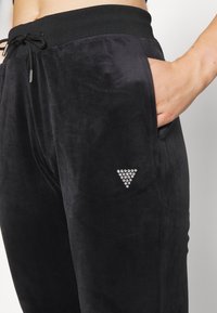 Zwarte velours joggingbroek met een elastische tailleband, voorzien van een zijzak en een driehoekig patroon van strassteentjes op het linkerbeen.