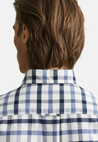 Baumwoll-Kariertes Hemd mit blau-weißem Karomuster, Knopfkragen und einer Schlaufe auf der Rückseite. Weiche Textur.