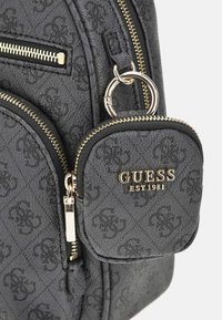 Schwarzer Stoffrucksack mit goldenen Beschlägen, versehen mit einer Reißverschlusstasche, geprägtem Muster und einer abnehmbaren Münztasche mit Logodetail.