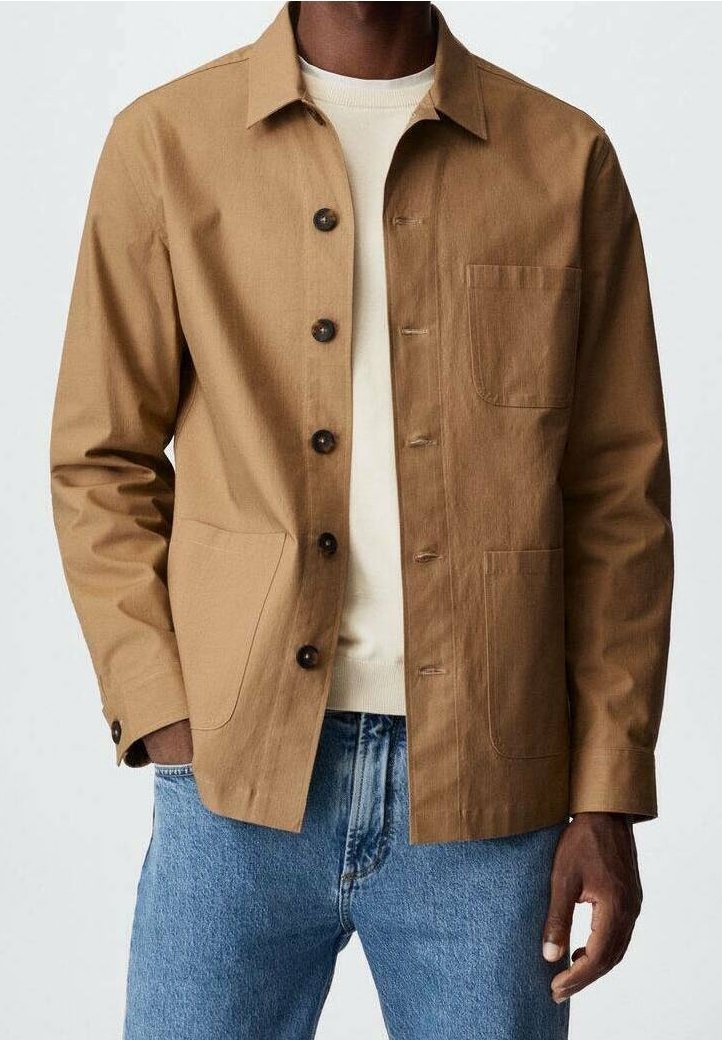 Veste marron boutonnée avec un col structuré, deux poches avant et un tissu texturé. Portée par-dessus un pull léger et un jean bleu.