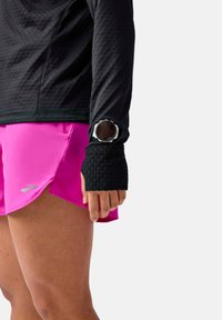 Black long-sleeve top with textured sleeves, paired with bright pink running shorts. A watch is worn on the wrist, with a silver bezel.