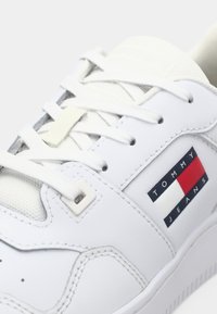 Baskets blanches Tommy Jeans avec lacets blancs et écusson logo rouge, blanc et bleu sur le côté.