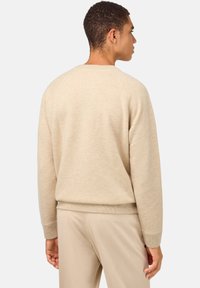 Bež sweatshirts, mehak tekstur, raglan rokavi, rebrasti manšeti in rob, sproščen kroj, prikazan zadaj, s prilegajočimi bež hlačami.