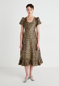 Žena v midi šatách s leopardím motívom a puffovými krátkymi rukávmi, ktorá stojí na pozadí v bielej farbe.