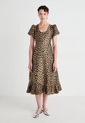 Woman wearing a leopard print midi dress with puffed short sleeves and silver Mary Jane flats, standing against a plain white background.