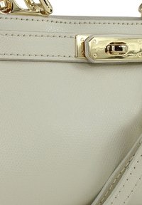 Lichtbeige leren handtas met een gestructureerde afwerking, goudkleurige hardware, een sluiting met gesp en stiksel langs de randen.