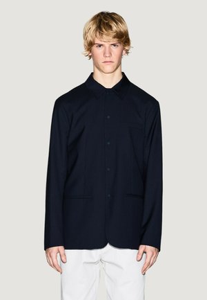 Giacca blu navy con bottoni, realizzata in un tessuto liscio, con colletto a punta, tasca frontale e tasche laterali. Design semplice con una vestibilità comoda.