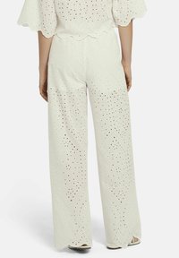 Witte wijde broek van oogjesstof met uitsnijdingen en een geschulpte zoom. Het ontwerp heeft geometrische accenten en een ontspannen pasvorm.