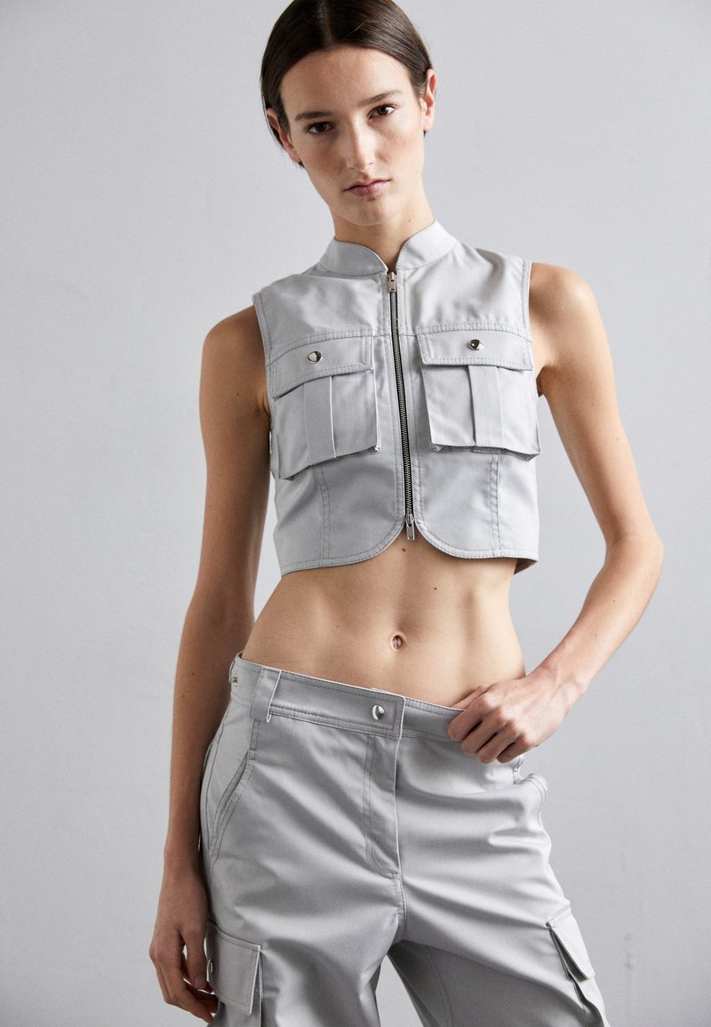 Gray cropped vest with a high collar, zip closure, and two front pockets. Paired with matching gray cargo pants featuring side pockets.