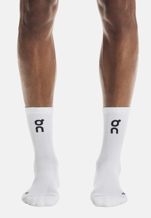 Piernas con calcetines blancos hasta la mitad de la pantorrilla con un logotipo negro "on" en cada lado, de pie contra un fondo blanco liso.